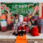 A woman sitting next to santa clause in front of many presents.