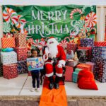 A child standing next to santa clause with presents.