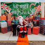 A person standing next to santa clause in front of many presents.