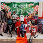 A group of people standing around santa clause.