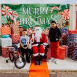 A man in santa suit sitting on the ground next to two kids.