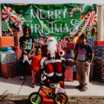 A group of people standing around santa clause on a bike.