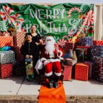 A man sitting in a santa claus chair next to two women.