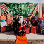 A man sitting next to santa clause in front of many presents.