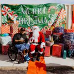 A man in a wheelchair sitting next to santa clause.