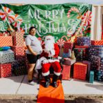 A woman standing next to santa clause in front of many presents.